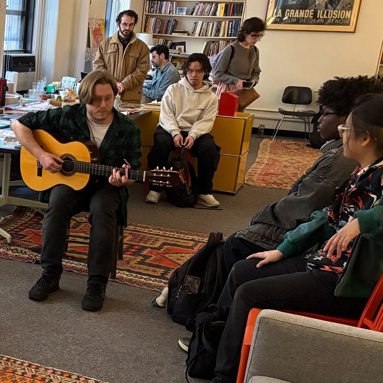 Students listen to another student play guitar in the Office of The Arts.