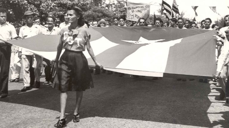 Parade carrying of Puerto Rican flag, Sign in the back reads “Ya Filipinas es libre. Y Puerto Rico?” (“The Philippines are already free. And Puerto Rico?”) Offices of the Government of Puerto Rico in the United States (OGPRUS) Records
