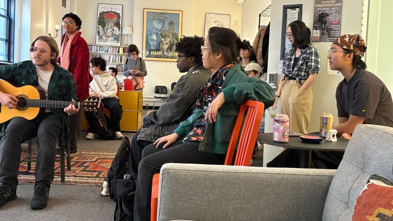 Students listening to another student play guitar and sing at an Arts Meet-Up