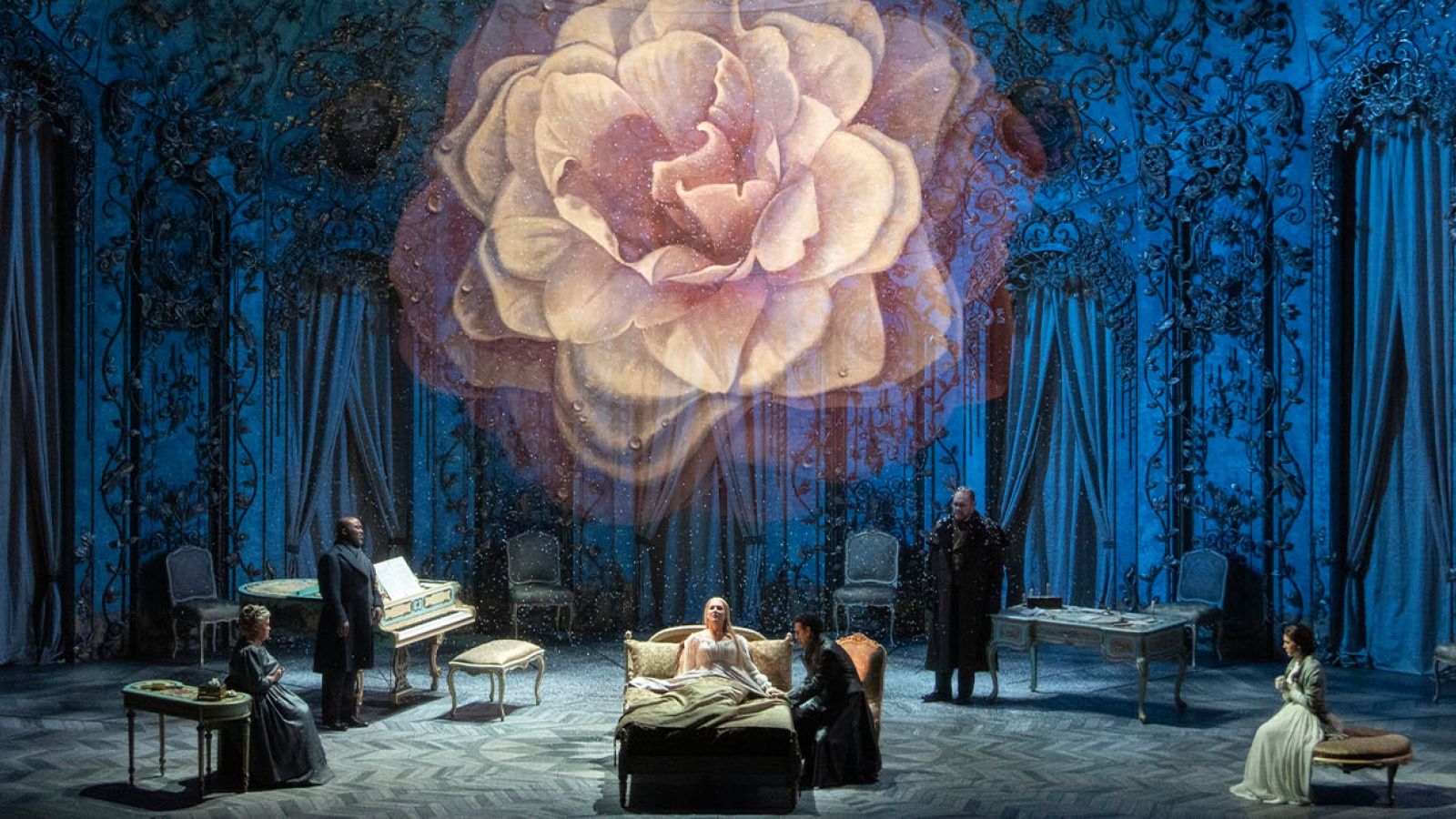 A large pink rose hangs above a dark forest with actors on stage.