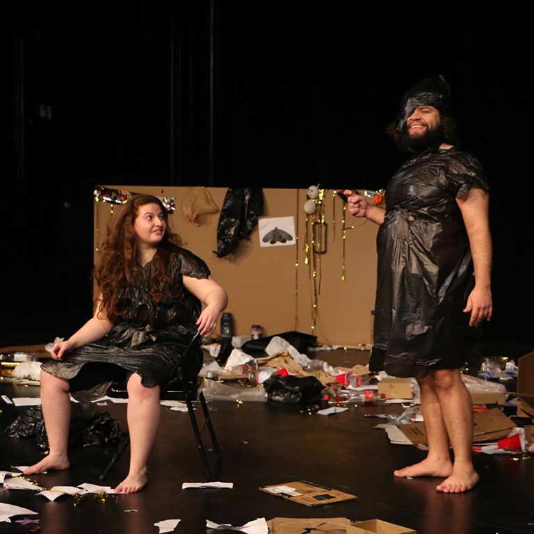Actors on stage wearing trash bags and smiling.