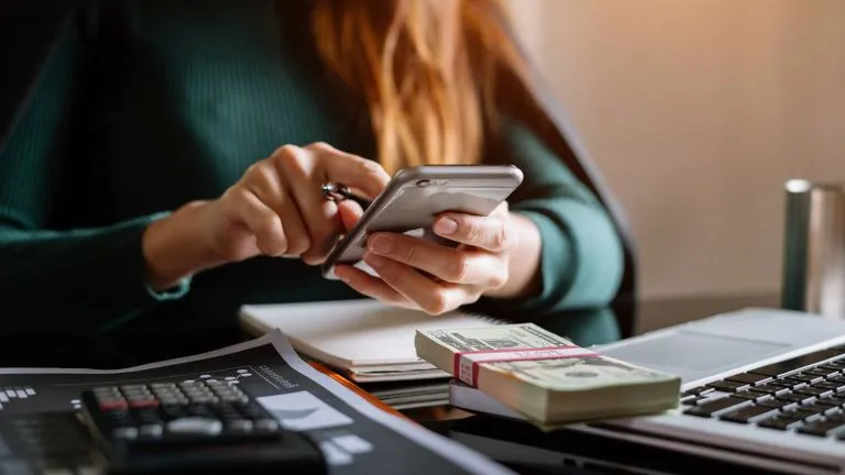Person typing on phone, infront of a desk with money on it