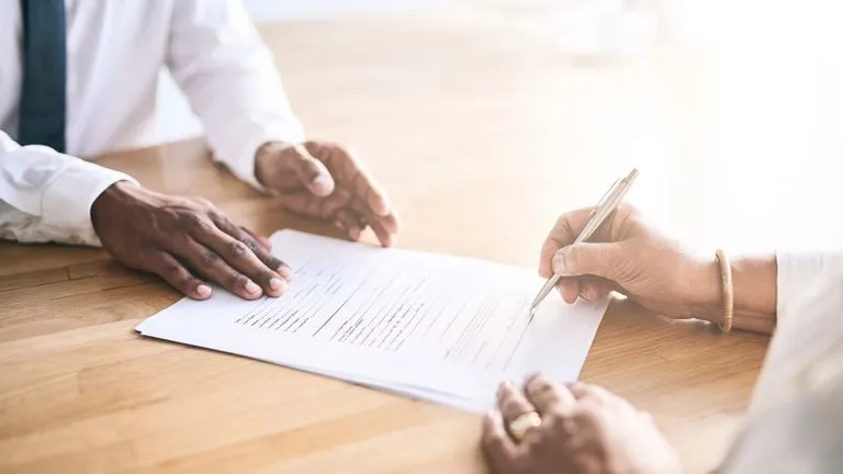 Two people at a desk with one of them signing a contract