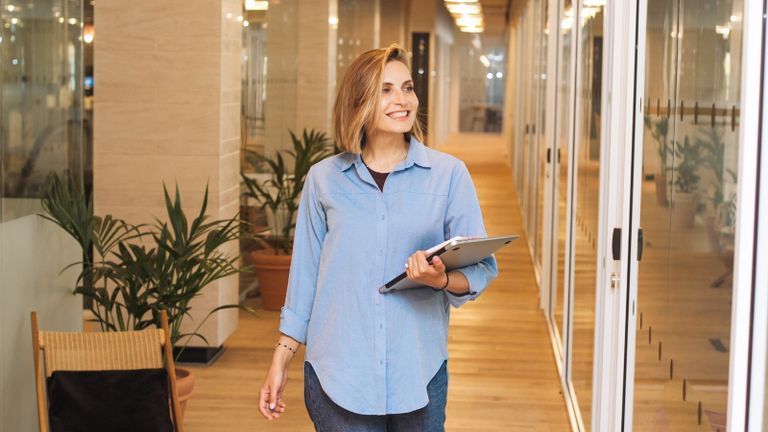 Photo - Young woman walking down a modern, well-lit hallway between glass walls