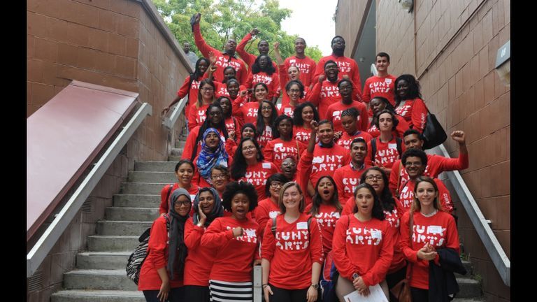 Students pose for photo on stairs in matching red CUNY Arts shirts.