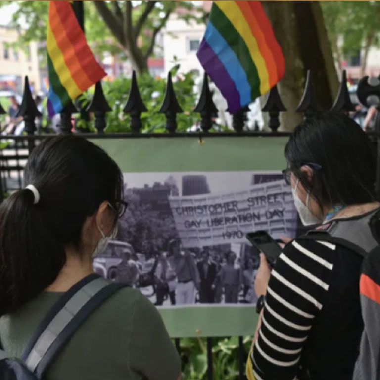 Two people standing in front of LGBTQ flags