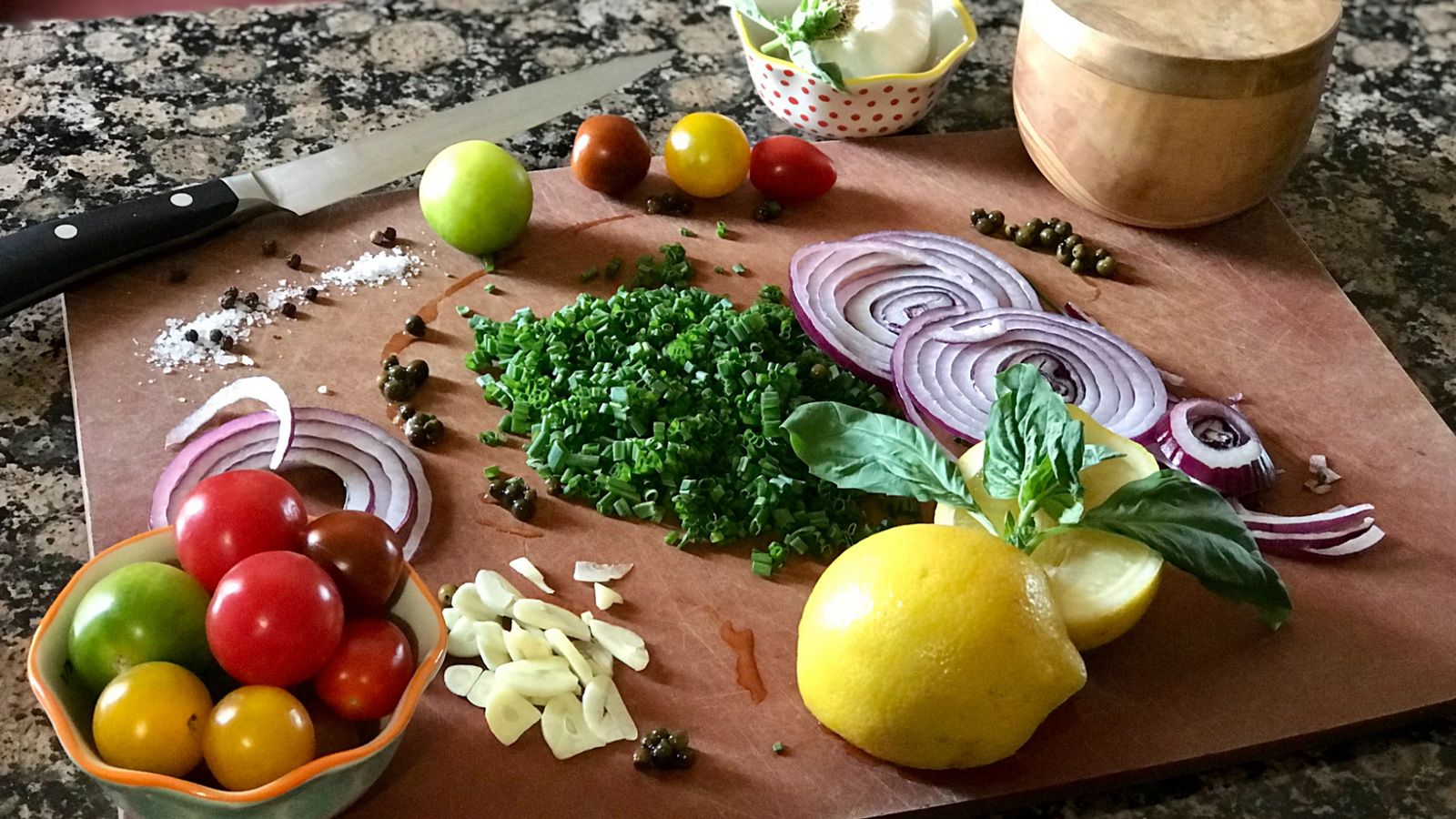 Photo of sliced onions, garlic, chives, and containers of other ingredients being prepared for cooking.