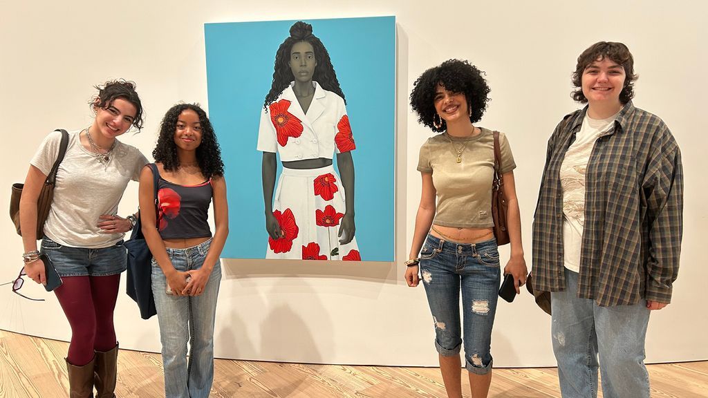 Four students smile in front of a painting at a museum