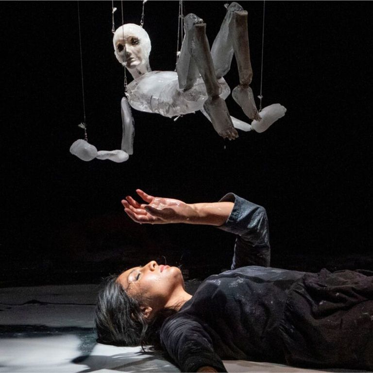 Actress lays down and reaches her hand up towards a puppet.
