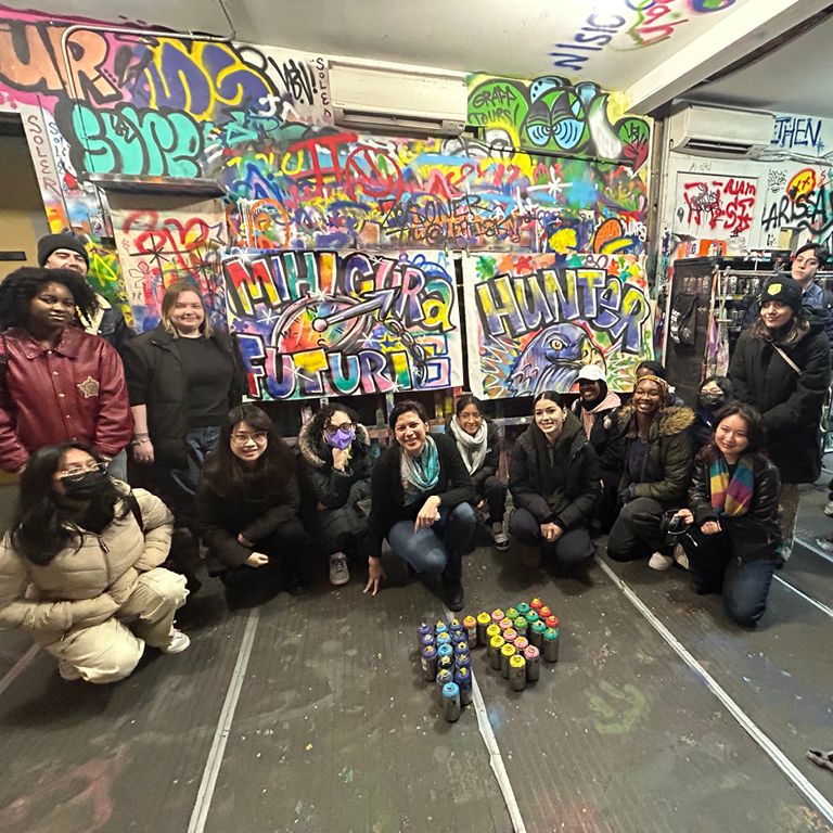 HUM 201 students pose in front of the graffiti they made on a class trip.
