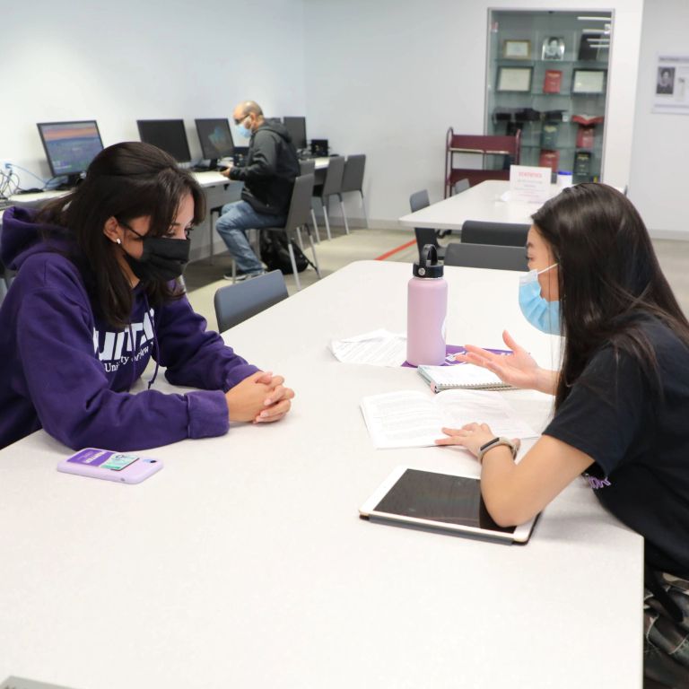 Two Hunter students discussing paperwork in the library.