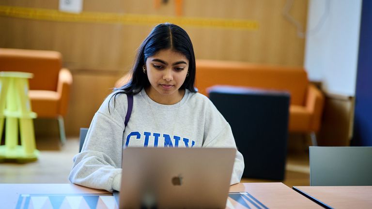 Hunter student wearing CUNY sweatshirt working on laptop in Student Union