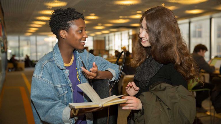 two hunter students smiling while looking at a book in the library