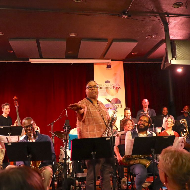 Conductor leads jazz band on stage.