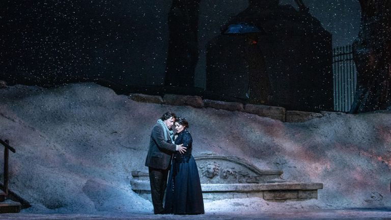 Opera singers hug on stage in the snow.