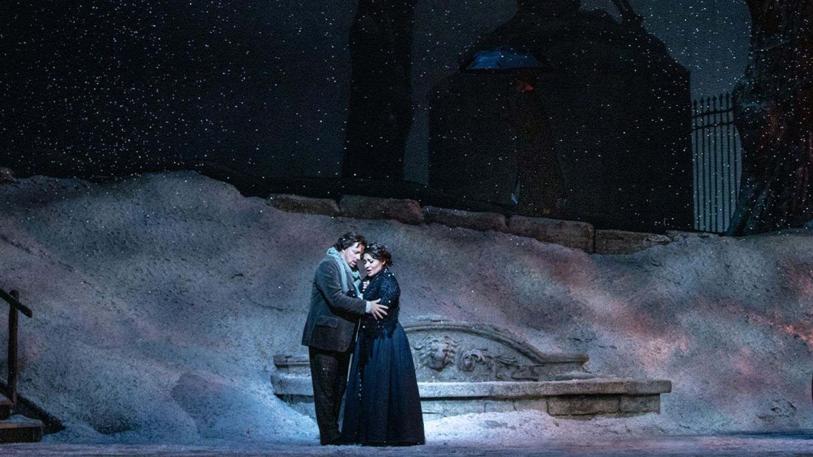 Opera singers hug on stage in the snow.