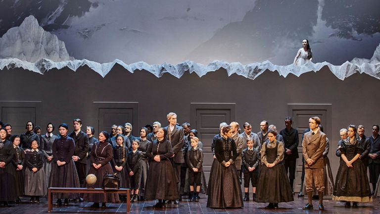Opera Singers on stages with matching uniforms, while a woman in white sits above them on a snow covered mountain.