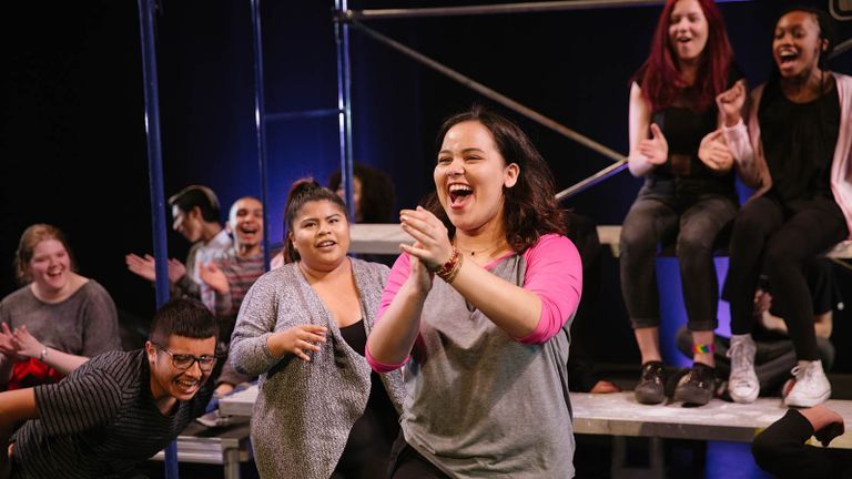 Young theater artists laughing and clapping on stage.