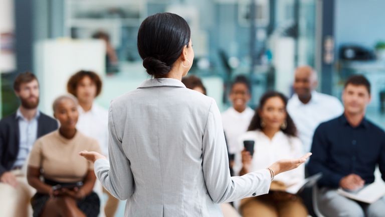 Photo of a woman addressing a small audience of seated adults.