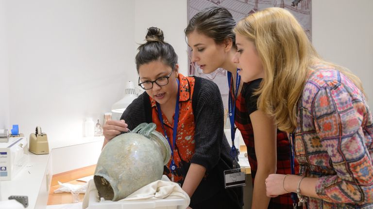 Three people talking and inspecting a vase.