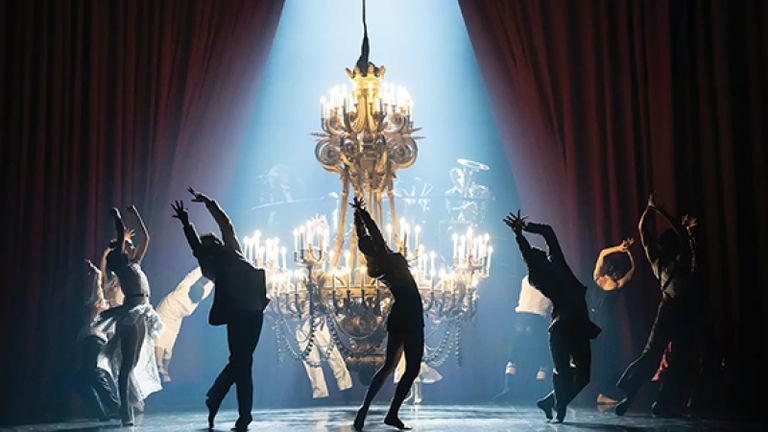 Silhouettes of performers dancing underneath a chandelier.