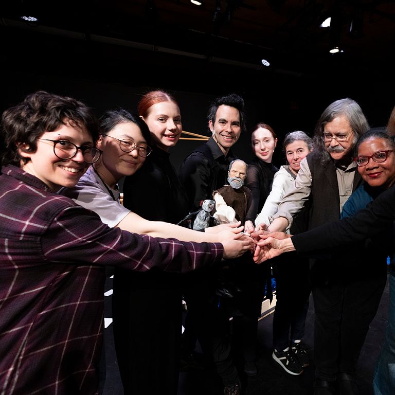 Interns in a circle with their hands place on top of each other smile for a photo.