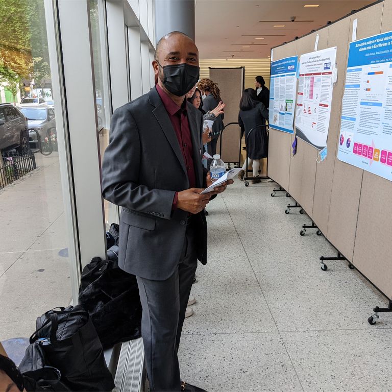 A person in a face mask in front of presentation boards.