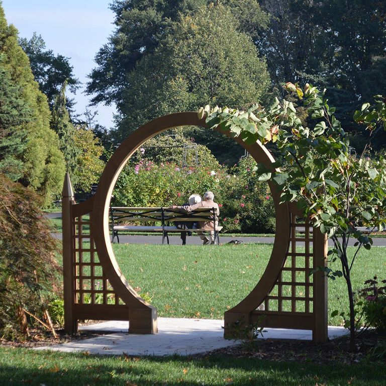 Two people sitting on a bench framed by an archway at the Queens Botanical Garden