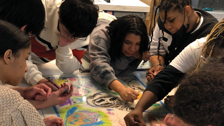 A group of artists in a circle drawing on the same paper.