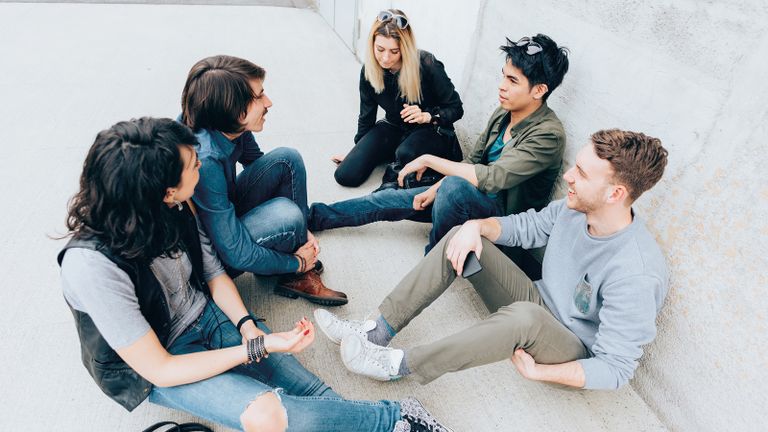 Photo of a group of students sitting and chatting with one student looking on