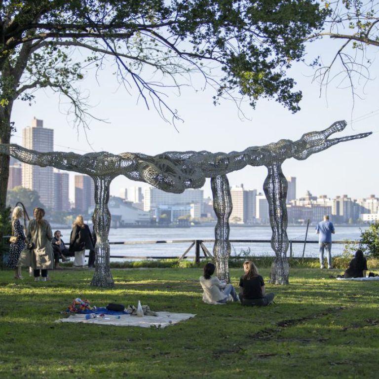 People sitting in the park next to a large metal crocodile sculpture