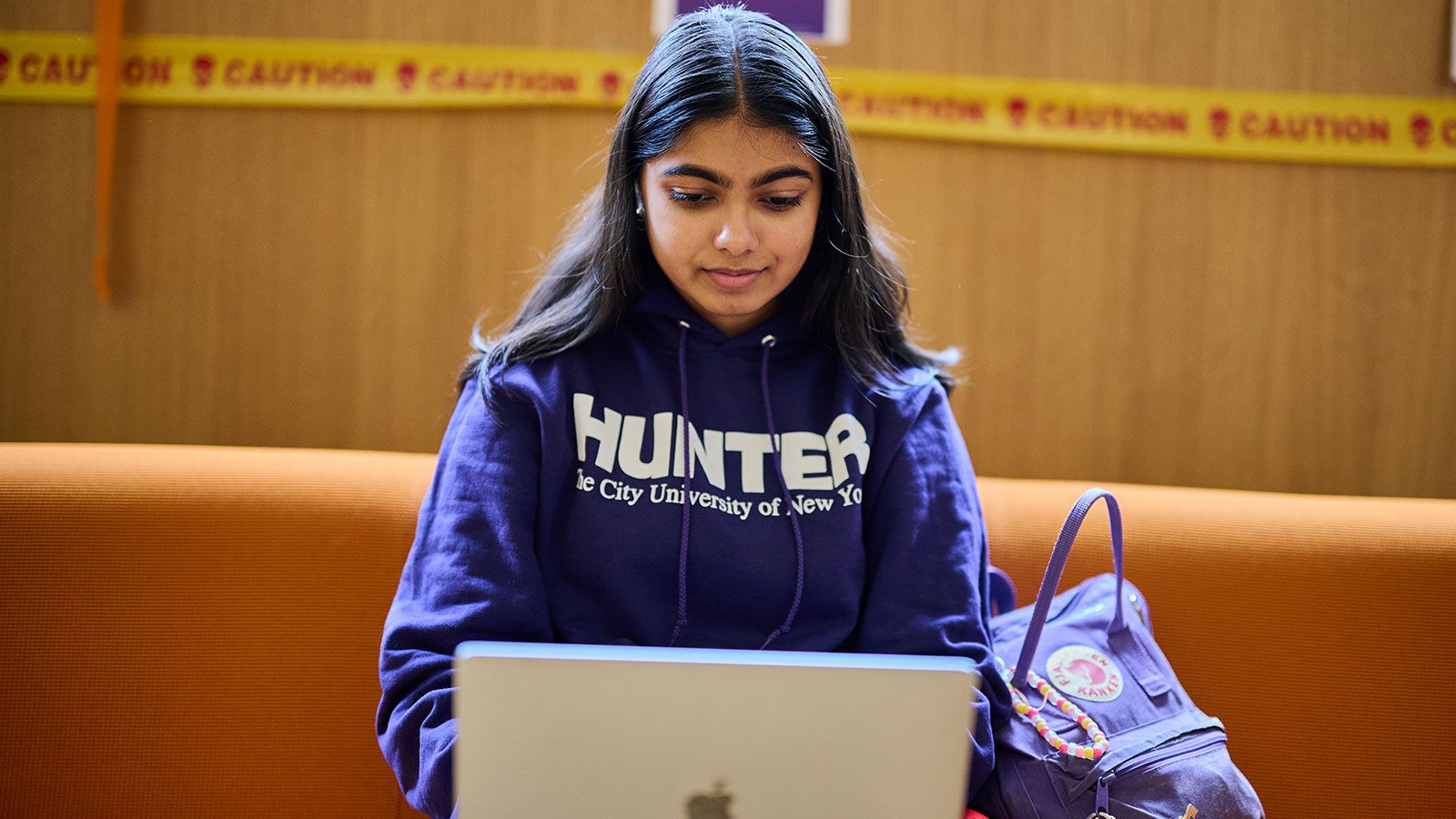 Hunter student wearing CUNY sweatshirt working on laptop in Student Union