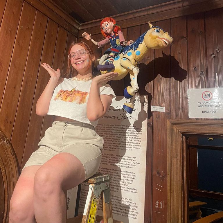 Student smiles and poses for picture in front of a marionette doll.