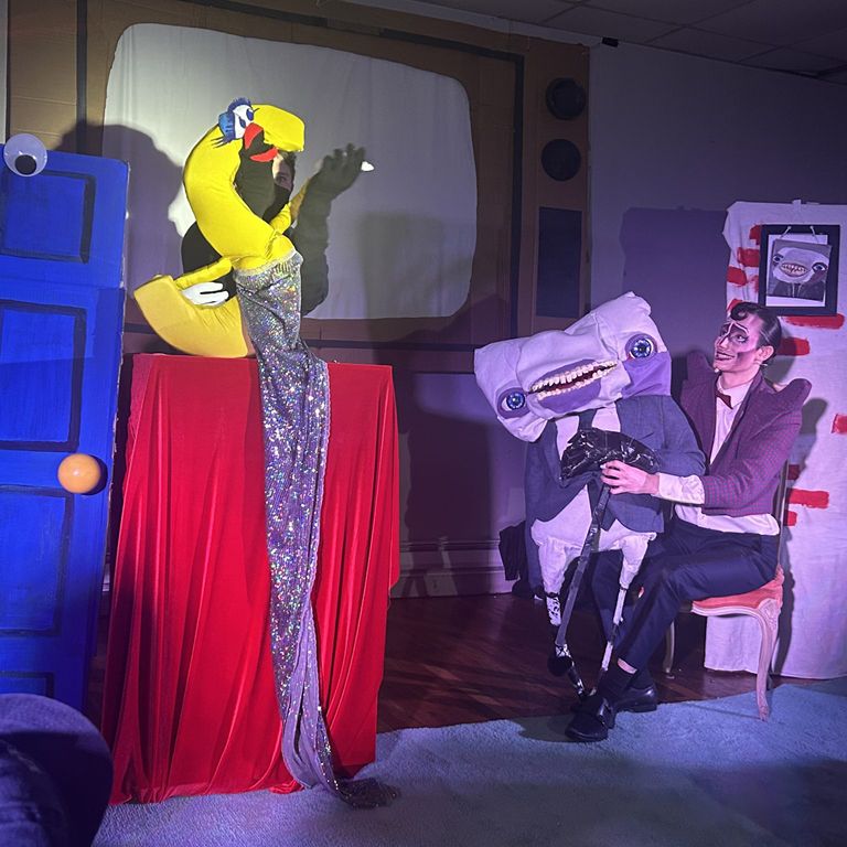 A performer on stage in drag with puppets.