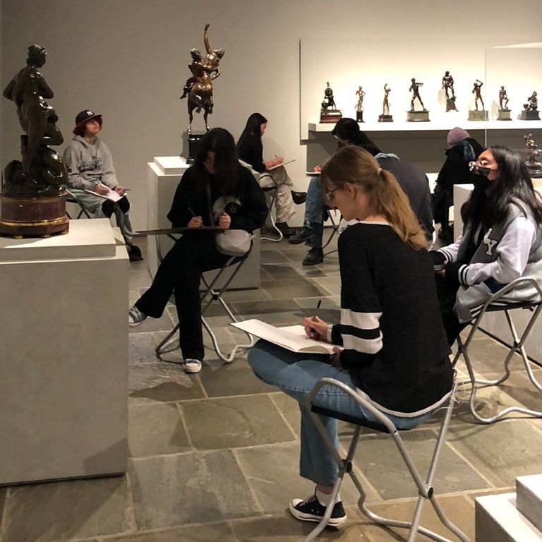 Student sitting in chairs and sketching artwork at the Frick