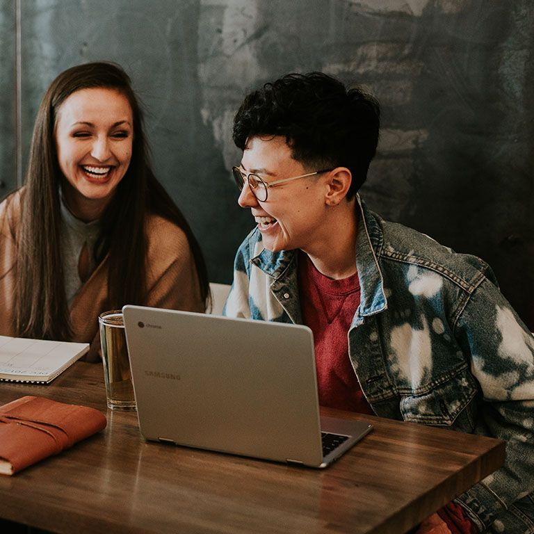 Two females laughing while working on computers