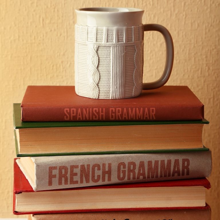 french and spanish grammar books stacked with a white mug on top