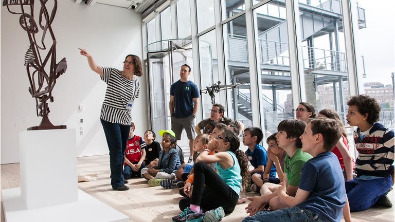Children looking at art while a teacher speaks.