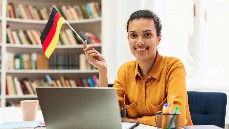 Woman holding a German Flag while sitting at a desk with a laptop.