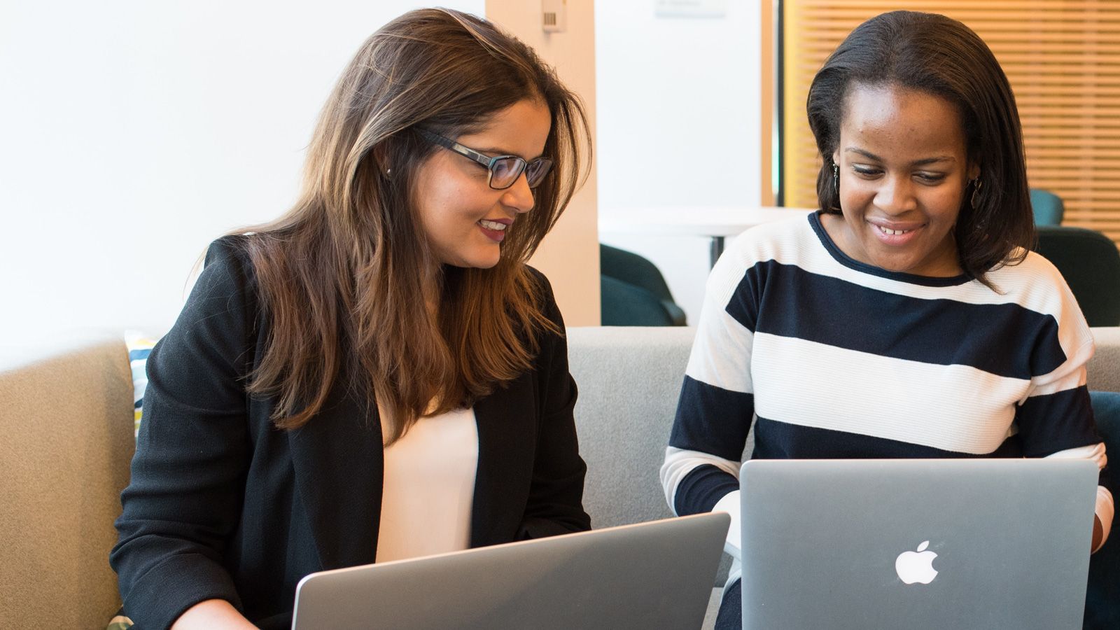 Photo - Two young women chatting and sharing their laptops