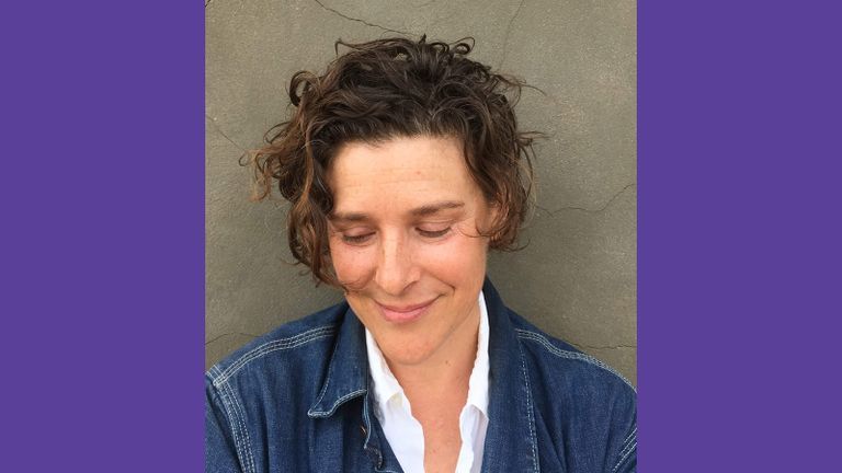 Photo of Zoe Leonard wearing a white dress shirt and jean jacket smiling and looking down.